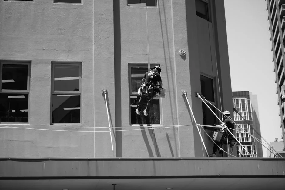 Un homme nettoie les vitres d’un gratte-ciel avec un harnais, illustrant un travail en hauteur en milieu urbain.