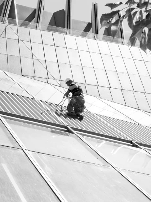Three window cleaners suspended on ropes clean a modern glass building facade during the day.